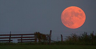 When the Moon is close above the horizon, the Moon illusion may cause it to appear larger, and Rayleigh scattering can impart a red color.[1]