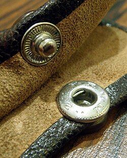 The two halves of a riveted leather snap fastener. The top half has a groove which "snaps" in place when "pressed" into the bottom half.