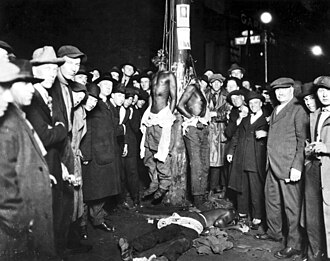 White men pose for a photograph of the 1920 Duluth, Minnesota lynchings. Two of the black victims are still hanging while the third is on the ground. Lynchings were often public spectacles for the white community to celebrate white supremacy in the U.S., and photos were often sold as postcards.[32]