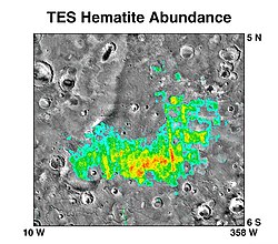 A grayscale map of an area on Mars (from 5° N to 6° S and from 10° W to 358° W (or 2° E), crossing 0° in both axes), with a false-color overlay (cyan, green, yellow, red) showing hematite abundance on the surface.