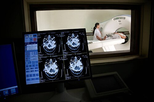 A radiologic technologist monitoring a patient during a head CT scan from the control room.