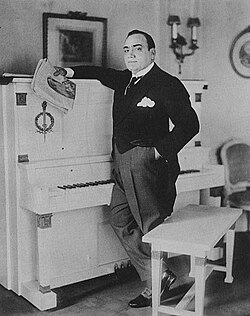 Caruso in front of his white Empire-style upright piano, in his apartment in New York City