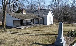 Jesse James Farm in Kearney, Missouri. The original farmhouse is on the left and an addition on the right was expanded after Jesse James died. Across a creek and up a hill on the right was the home of Daniel Askew who was killed at home on April 12, 1875. Askew was suspected of cooperating with the Pinkertons in the January 1875 bombing of the house (in a room on the left). James's original grave was on the property but he was later moved to a cemetery in Kearney. The original footstone is still outside although the family has replaced the headstone.