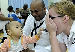 US Navy sailors play peek-a-boo with a child in the Children's Ward at Hospital Likas.