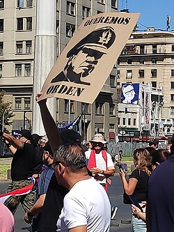 Pro–Pinochet protester holding a sign with Pinochet's face that says "We want order" in May 2023. In the background, there is another sign with Allende's face.