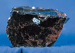 Obsidian with a conchoidal fracture, some weathering, and rust-red coloring. Obsidian is volcanic glass; often black and opaque.