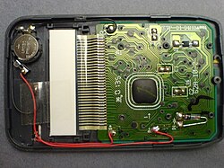 The interior of a pocket calculator. The dark lump of epoxy in the center covers the processor chip
