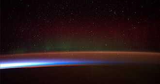Earth's night-side upper atmosphere appears from the bottom as bands of afterglow illuminating the troposphere in orange with silhouettes of clouds at the top, and the stratosphere in white and blue at the top of the middle. Next, the mesosphere (pink area) extends to the orange and faintly green line of the lowest airglow, at about one hundred kilometres at the edge of space and the lower edge of the thermosphere (invisible). Continuing with green and red bands of auroras stretching over several hundred kilometres.