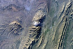 Astronaut photo of the southwestern edge of the Zagros Mountains featuring the Jashak salt dome (white spot in center). Erosion revealed the uplifted tan and brown rock layers surrounding the salt dome to the northwest and southeast (center of image). Radial drainage patterns indicate another salt dome is located to the southwest (image left center).