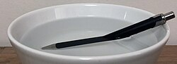 A pen partially submerged in a bowl of water appears bent due to refraction at the water surface.