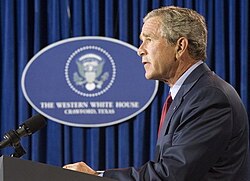 President George W. Bush speaks to the press from his Crawford, Texas ranch on Sunday August 28, 2005. The logo in the background was created by the Bush administration in August 2001, and it was displayed at press briefings during Bush's stays at his ranch in Crawford. The sign reads:THE WESTERN WHITE HOUSECRAWFORD, TEXAS