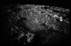 An oblique, black-and-white view of a portion of Mare Orientale from the CSM, illustrating the illuminating effect of Earthlight on the lunar terrain below during local nighttime; Evans reported seeing a light "flash" apparently originating from the surface in this area