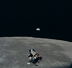 Lunar Module Eagle, the Lunar Module ascent stage of Apollo 11, in orbit above the Moon. Earth is visible in the distance. Photograph by Michael Collins aboard the Command module Columbia.