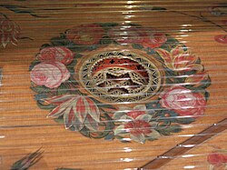 Detail of the harpsichord by Karl Conrad Fleischer; Hamburg, 1720 in Museu de la Música de Barcelona. A decorative rose descends below the soundboard in which it is mounted; the soundboard itself is adorned with floral painting around the rose. The bridge is at lower right.