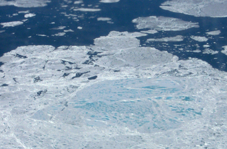 Aerial photograph showing a section of sea ice. The lighter blue areas are melt ponds and the darkest areas are open water; both have a lower albedo than the white sea ice, so their presence increases local and global temperatures, which helps to spur more melting
