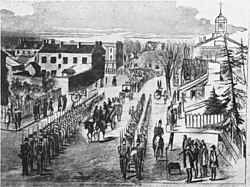 Brown sits on his coffin on his way to the gallows. Soldiers line up on both sides, to avoid a rescue.
