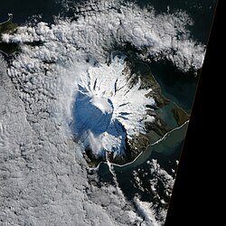 Satellite view of a snow-covered volcanic island partly surrounded by clouds