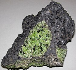 Green xenoliths of peridotite from the mantle are surrounded by black volcanic lava. These peridotite xenoliths were carried upward from the mantle by molten magma during a volcanic eruption in Arizona.