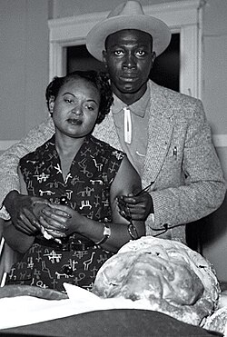 Till's mother looks over his mutilated corpse. With her is her fiancé Gene Mobley. Mamie Till had insisted on an open-casket funeral. Images of Till's body, printed in The Chicago Defender and Jet magazine, made international news and directed attention to the oppression of blacks in the U.S. South.