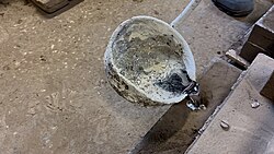 Molten metal in a crucible poured into sand form, with surface oxidation and residue typical of the casting process.