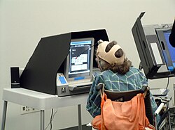 This voter with a manual dexterity disability is making choices on a touchscreen with a head dauber.