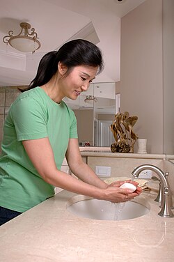 A woman washes her hands with soap and water.