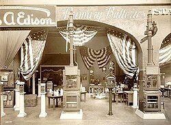 An exhibit in greyscale displays many objects on pylons. The background is draped in stars and stripes.