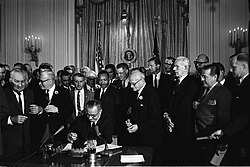 U.S. president Lyndon B. Johnson signs the Civil Rights Act of 1964. Among the guests behind him is Martin Luther King Jr.