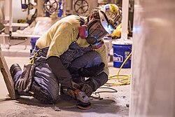 A worker grinds concrete flooring to prepare it for an epoxy coating. He wears a respirator to avoid breathing in silica dust, which causes silicosis and lung cancer.